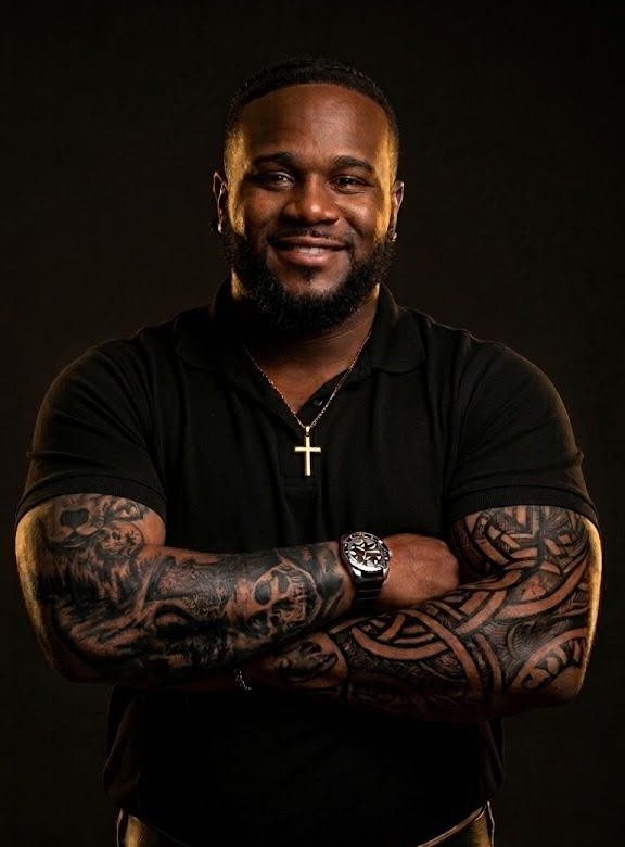 Raysean Thomas, owner of Team Thomas Services LLC, in a black company polo with both tattooed forearms crossed.